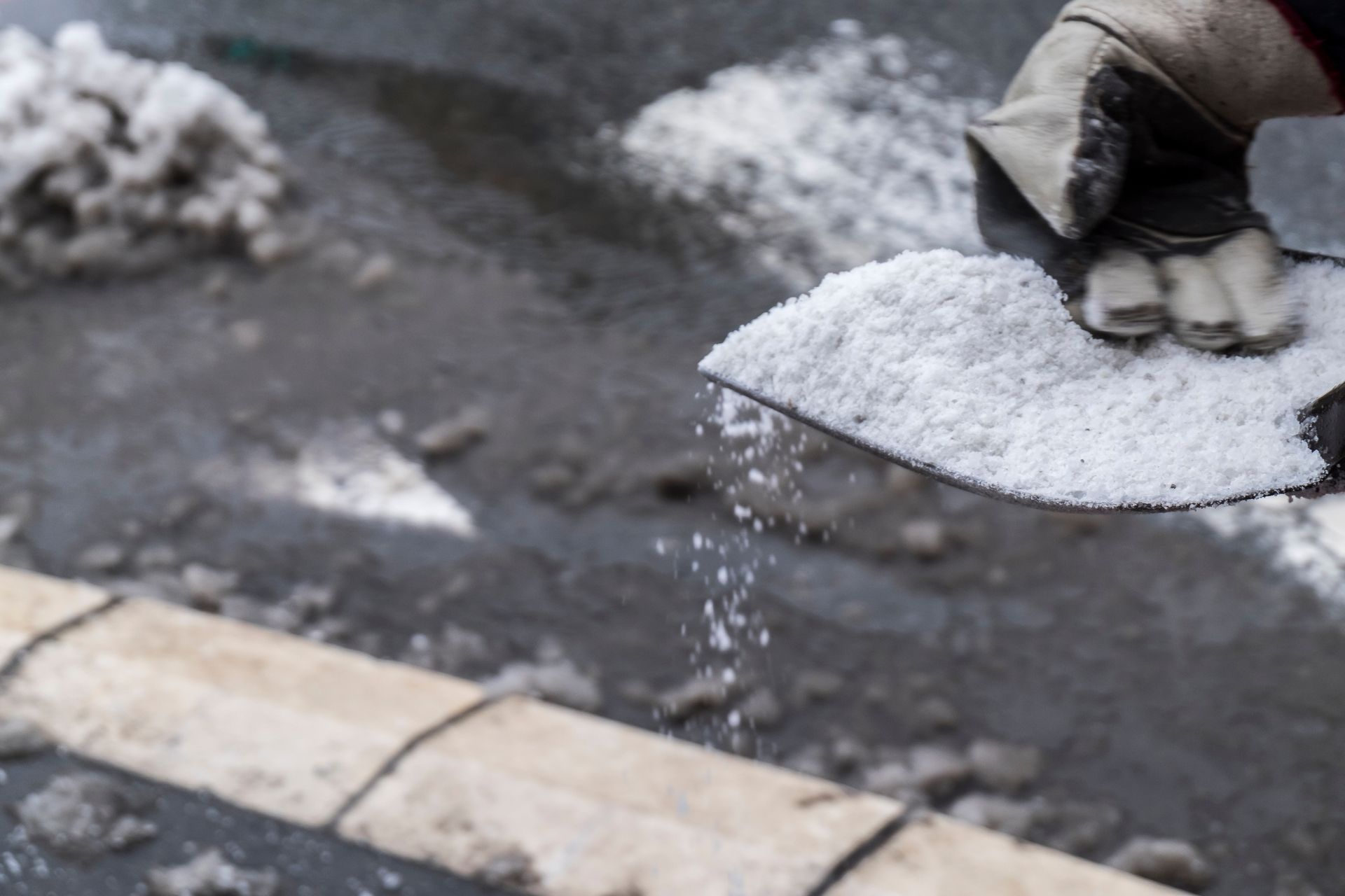 Person in gloves spreading salt on a snow-covered surface with a shovel.