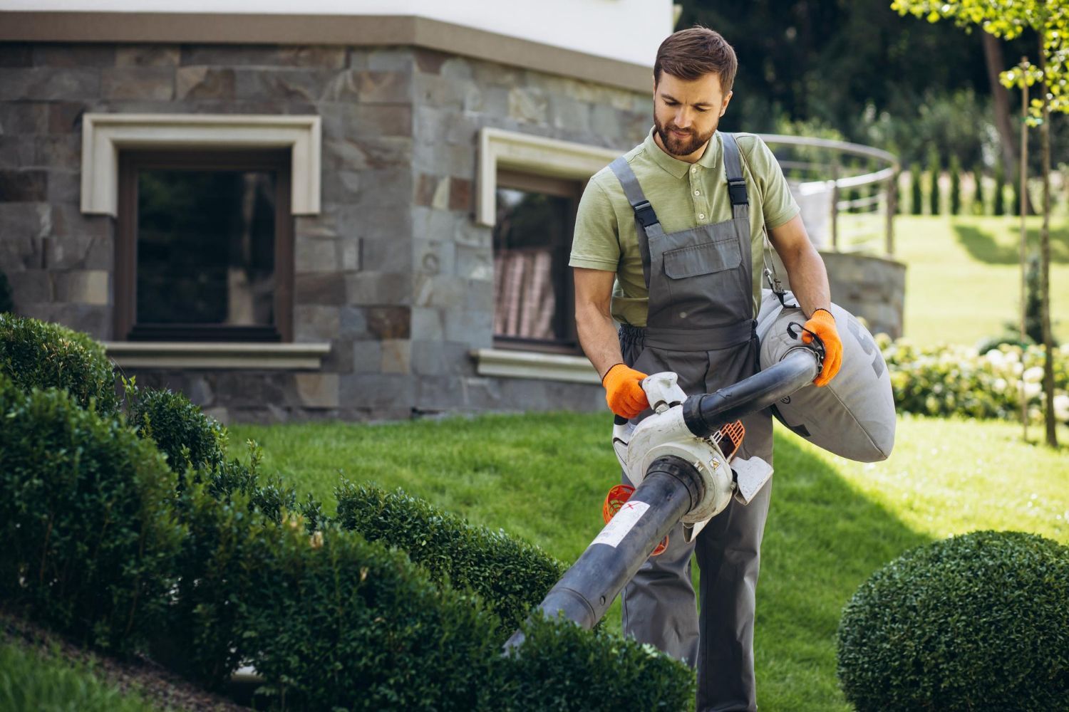 A man is using a vacuum cleaner to clean the grass in front of a house.