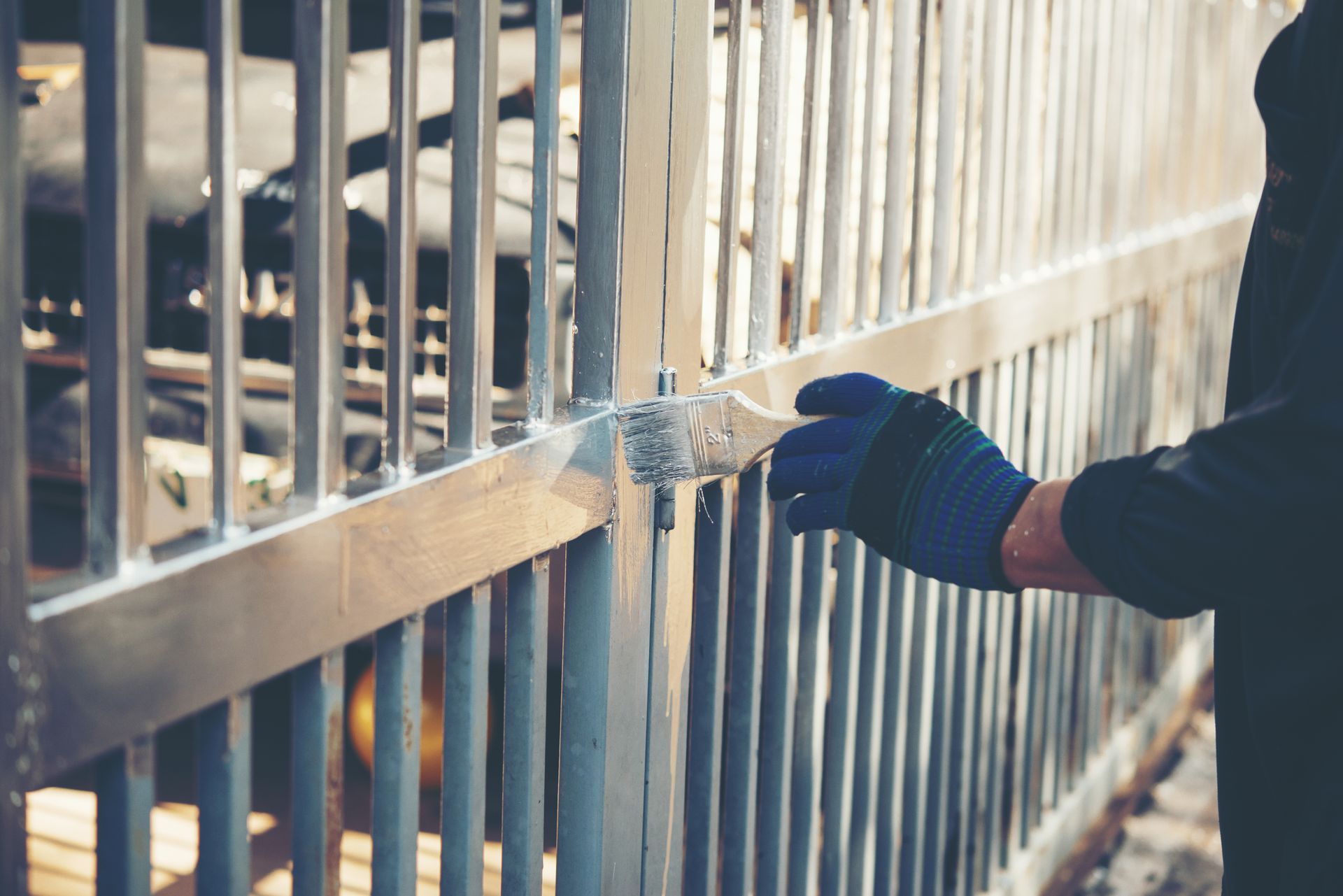 A man is painting a metal fence with a brush.