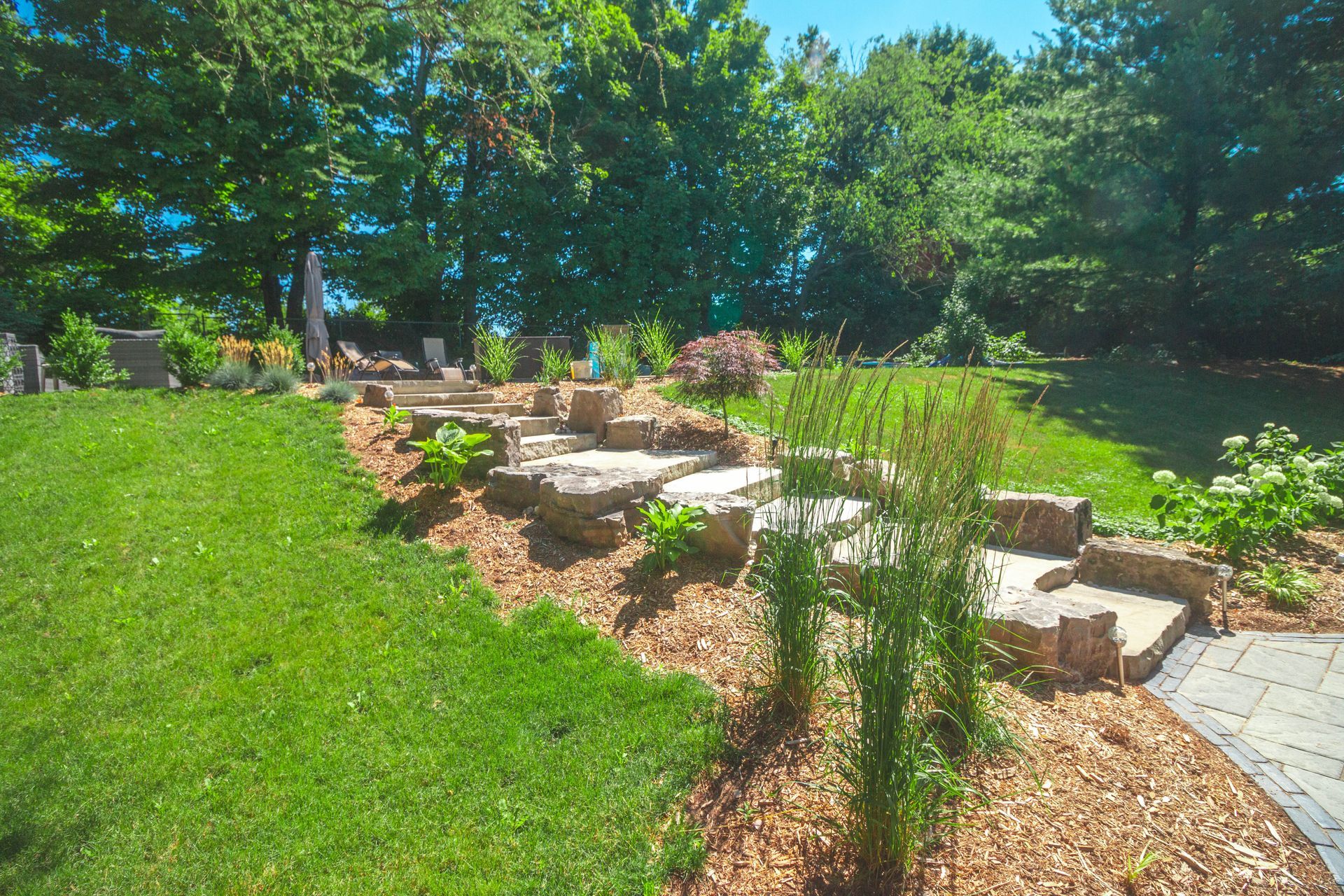 A lush green lawn with stairs leading up to a patio and trees in the background.