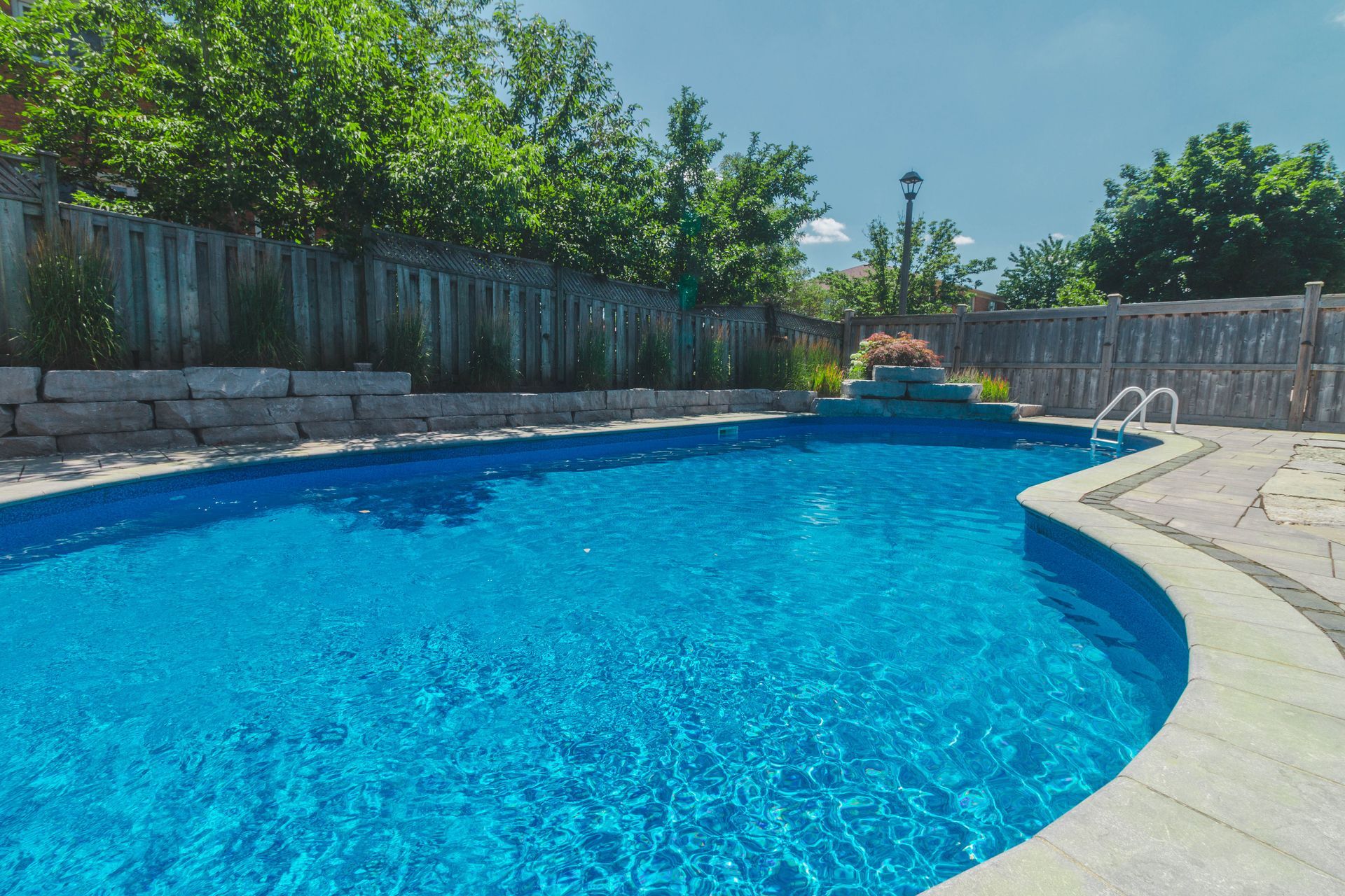 A large swimming pool is surrounded by trees and a fence.