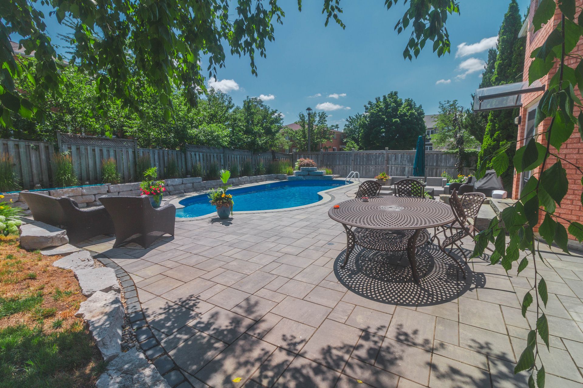 There is a large swimming pool in the backyard with a table and chairs.