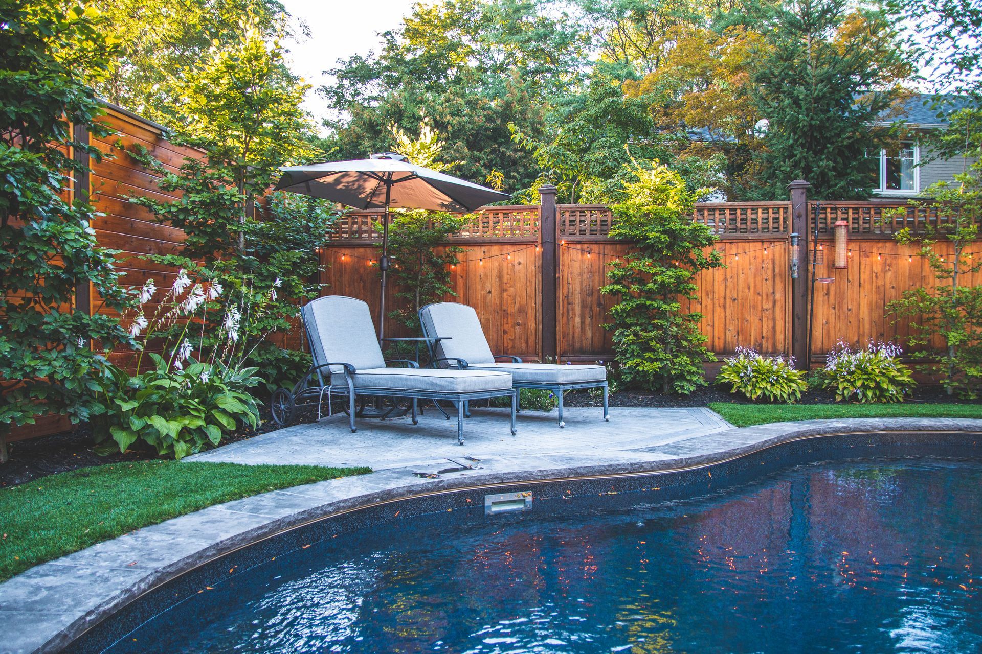 A swimming pool with two lounge chairs and an umbrella in the backyard.