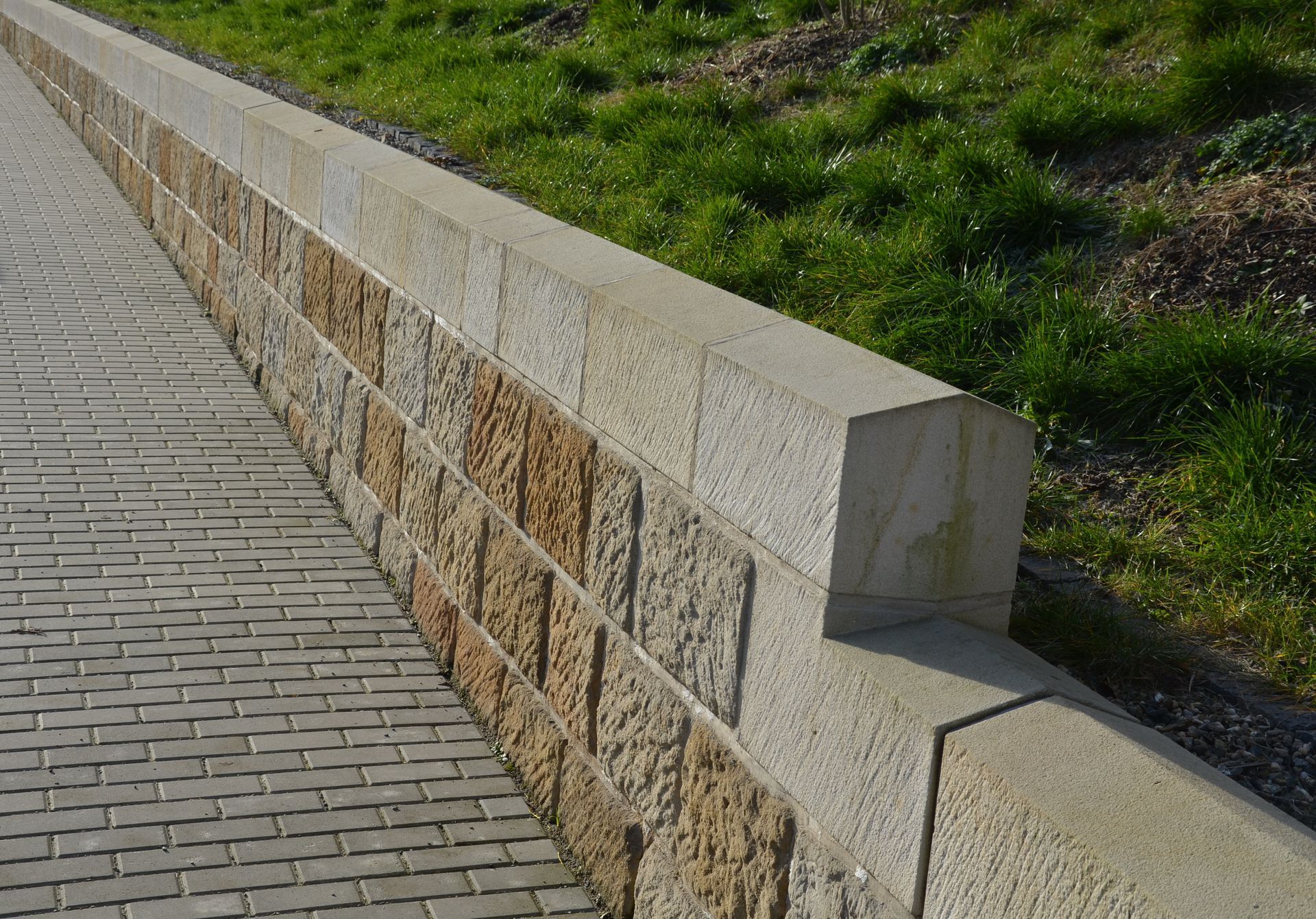 A stone wall along a sidewalk with grass in the background