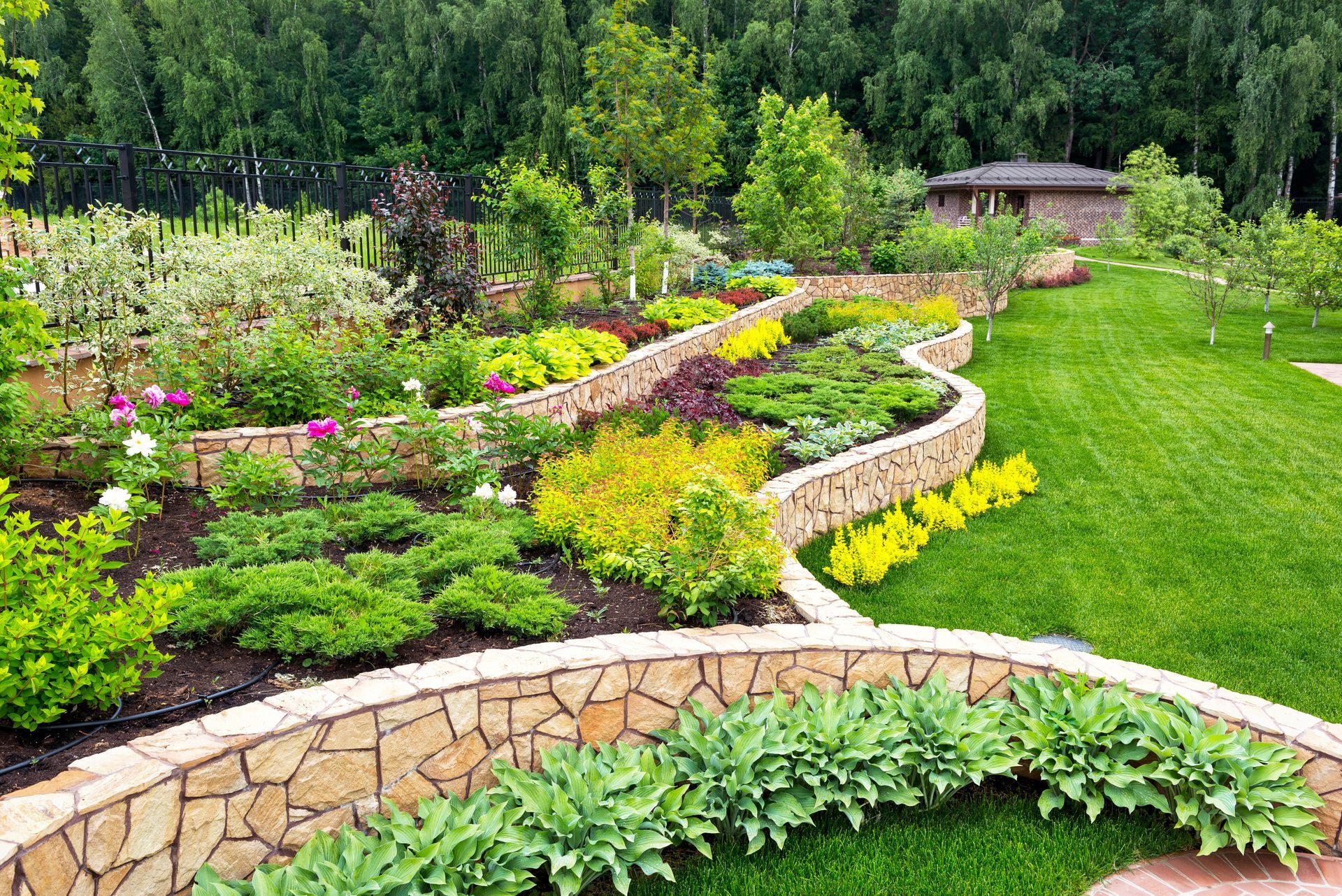 A garden with lots of plants and flowers and a stone wall.