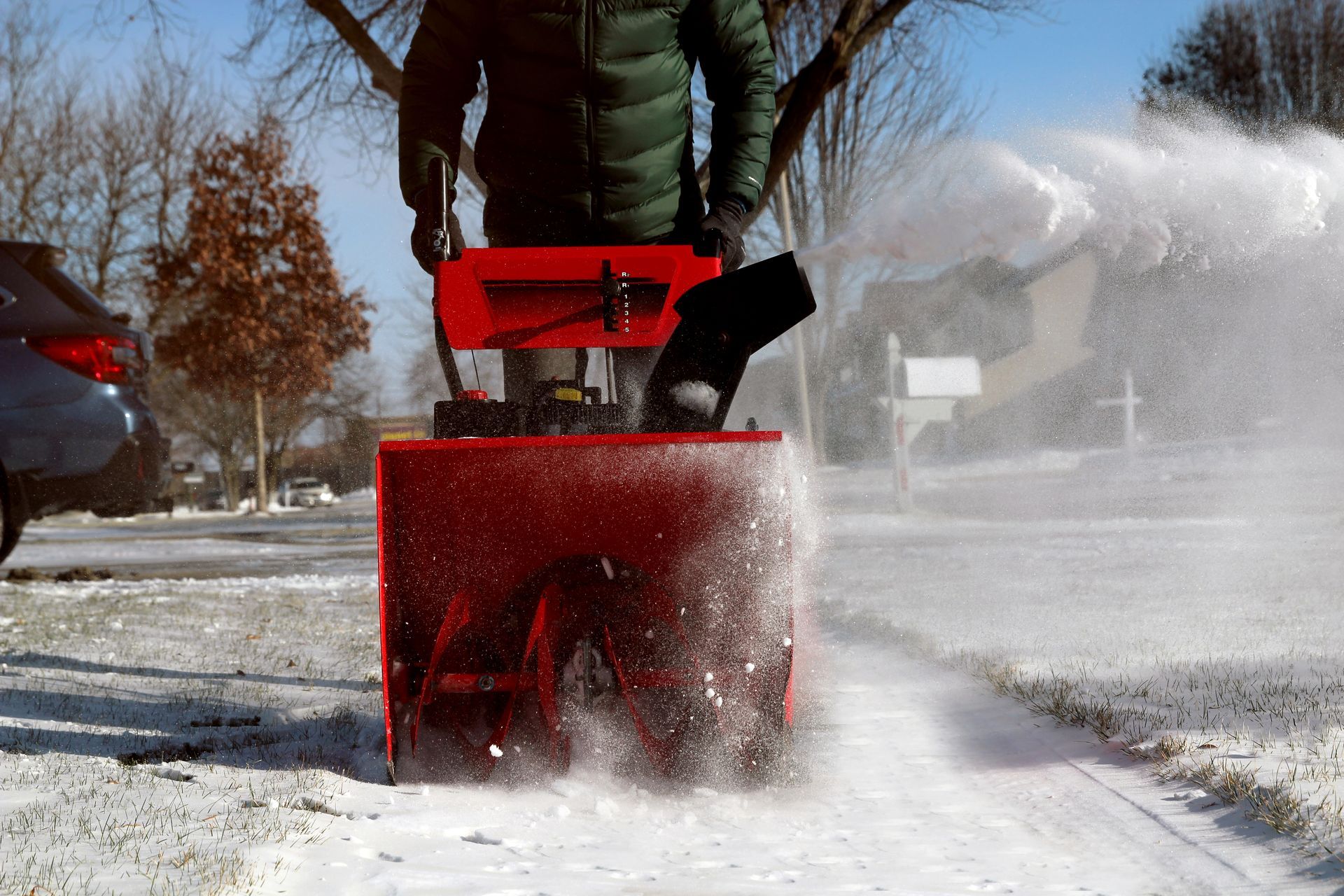 A man is using a snow blower to remove snow from the sidewalk.