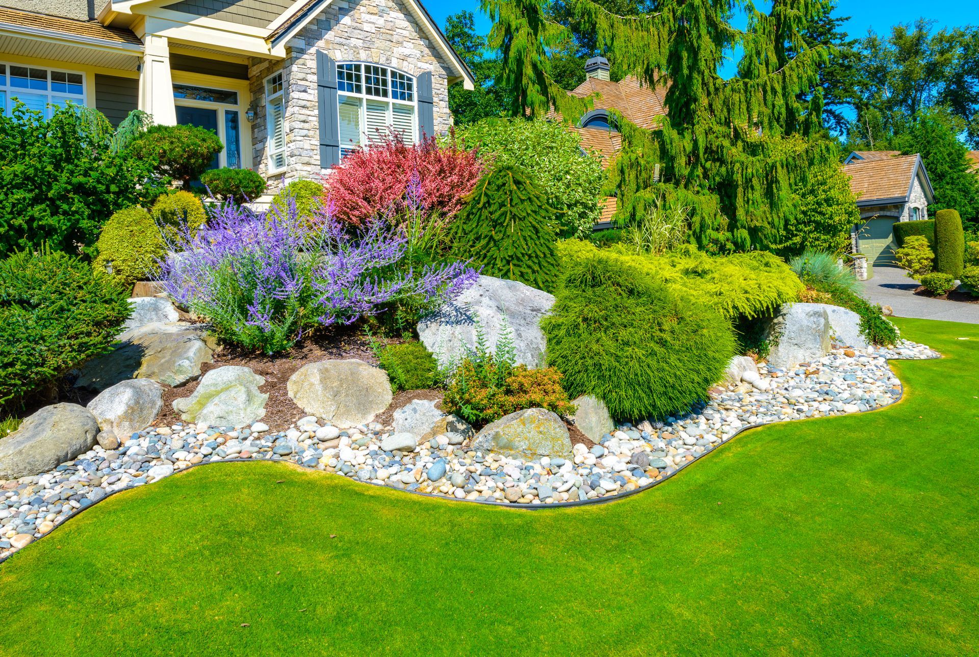 A house with a lush green lawn and a rock garden in front of it.