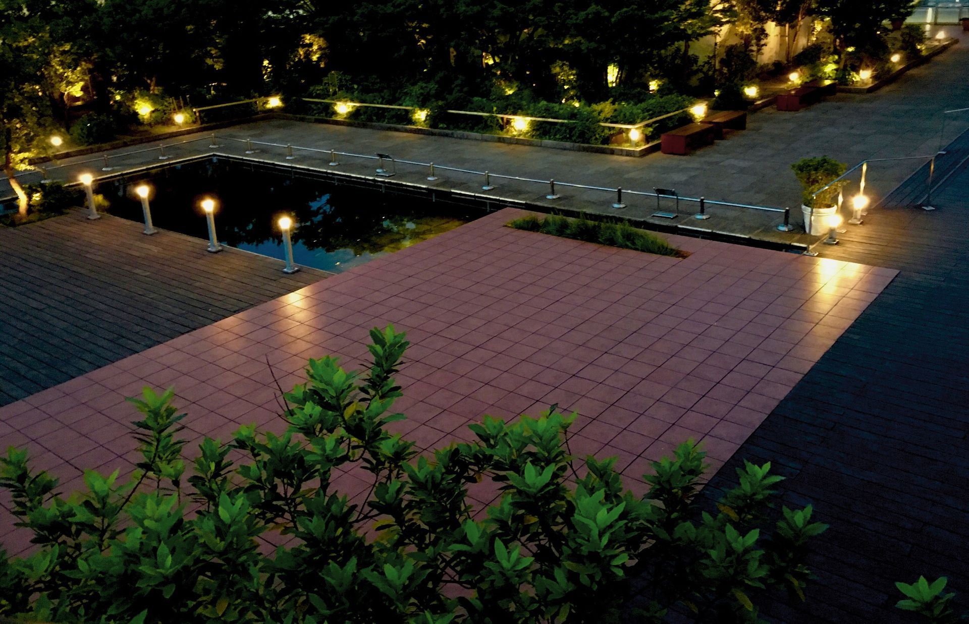 A brick walkway is lit up at night with a pond in the background