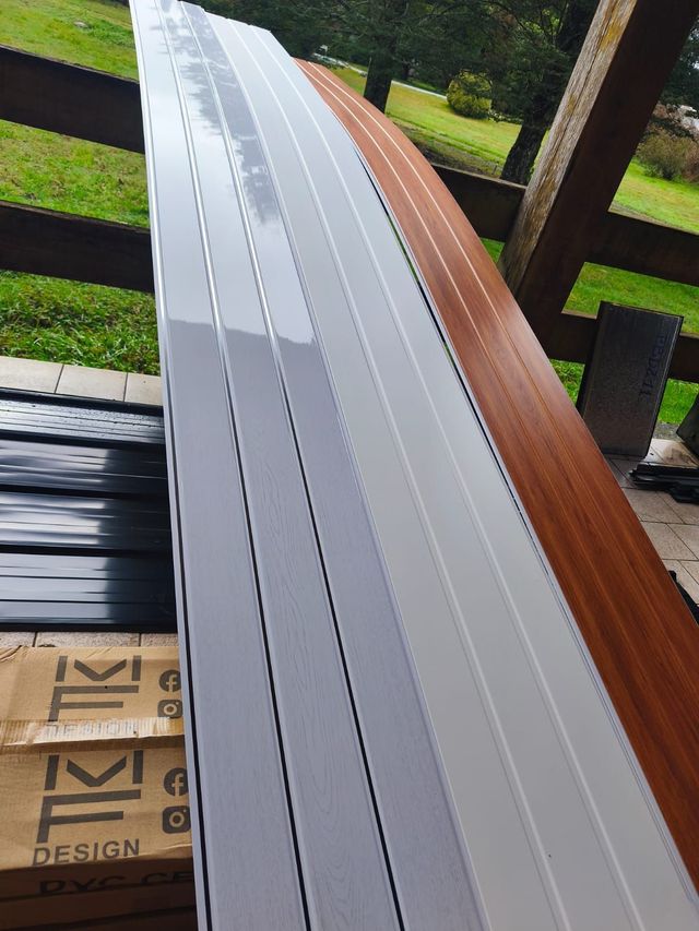 Un largo panel exterior de listones blancos y de madera, apoyado sobre una terraza con césped verde al fondo.