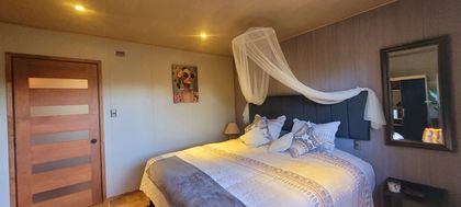 Habitación acogedora con cama, dosel blanco, espejo de pared y puerta de madera con iluminación cálida.
