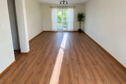 Habitación vacía con suelo de madera, paredes blancas y luz solar que entra por una ventana.