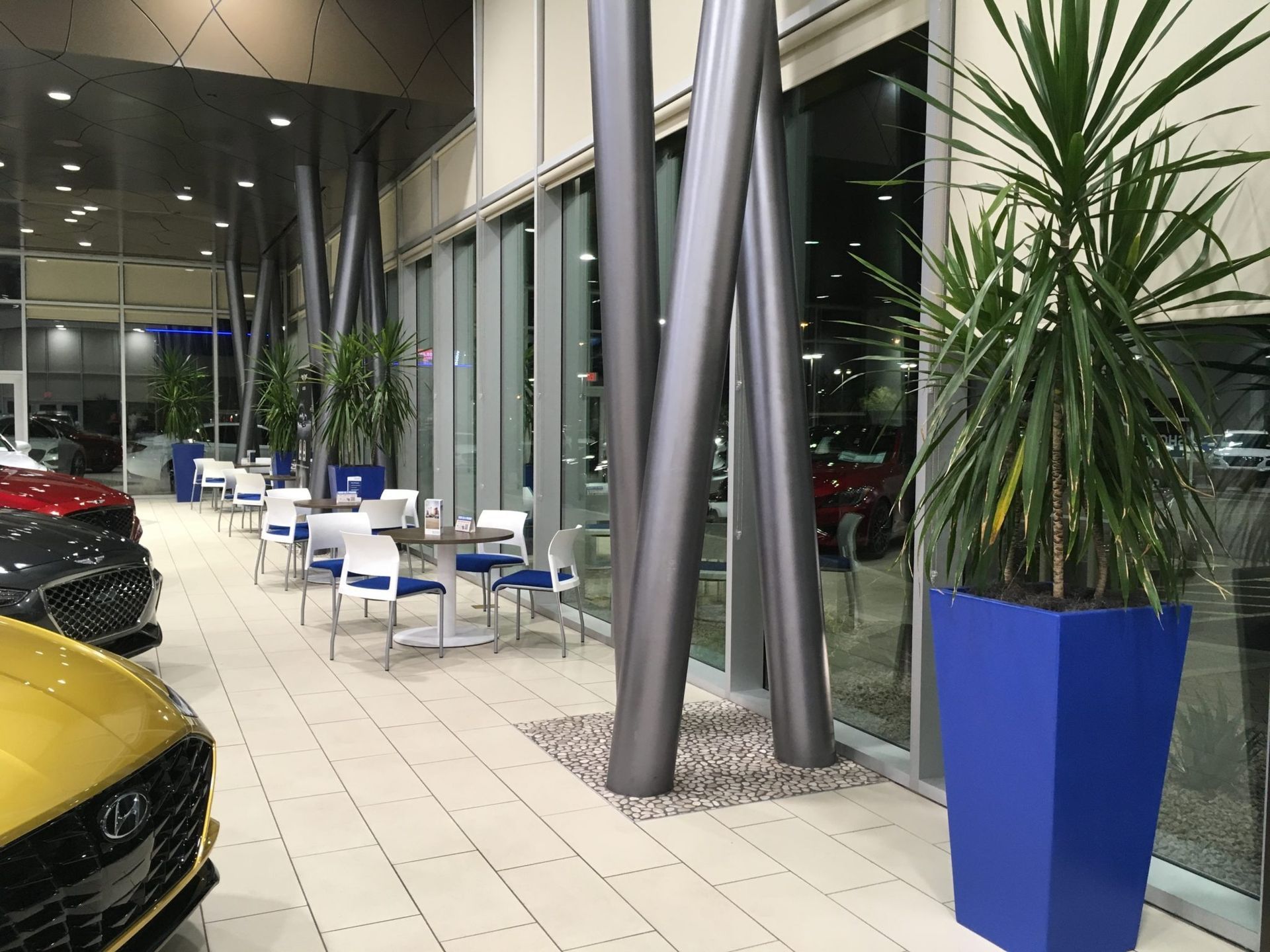 Car showroom interior with seating area, large windows, and a yellow Hyundai in the foreground.
