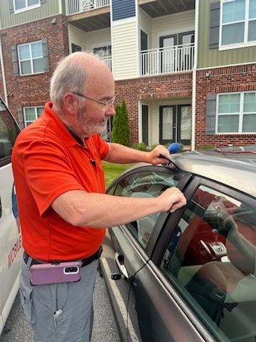 Man in orange shirt unlocking a car door; apartment building background.