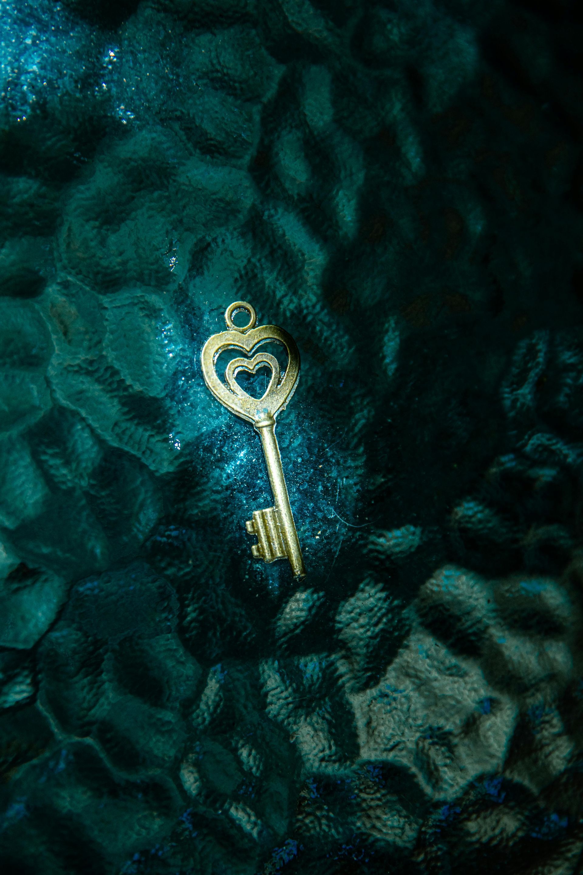 Golden key with heart-shaped details, sparkling against a textured teal surface.