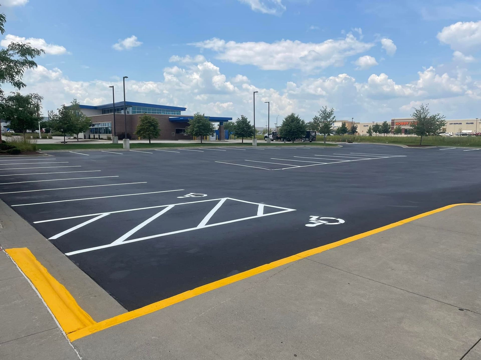 Newly paved asphalt driveway leading to a white building, lined with green grass and trees under a cloudy sky. Newly paved asphalt driveway leading to a white building, lined with green grass and trees under a cloudy sky.