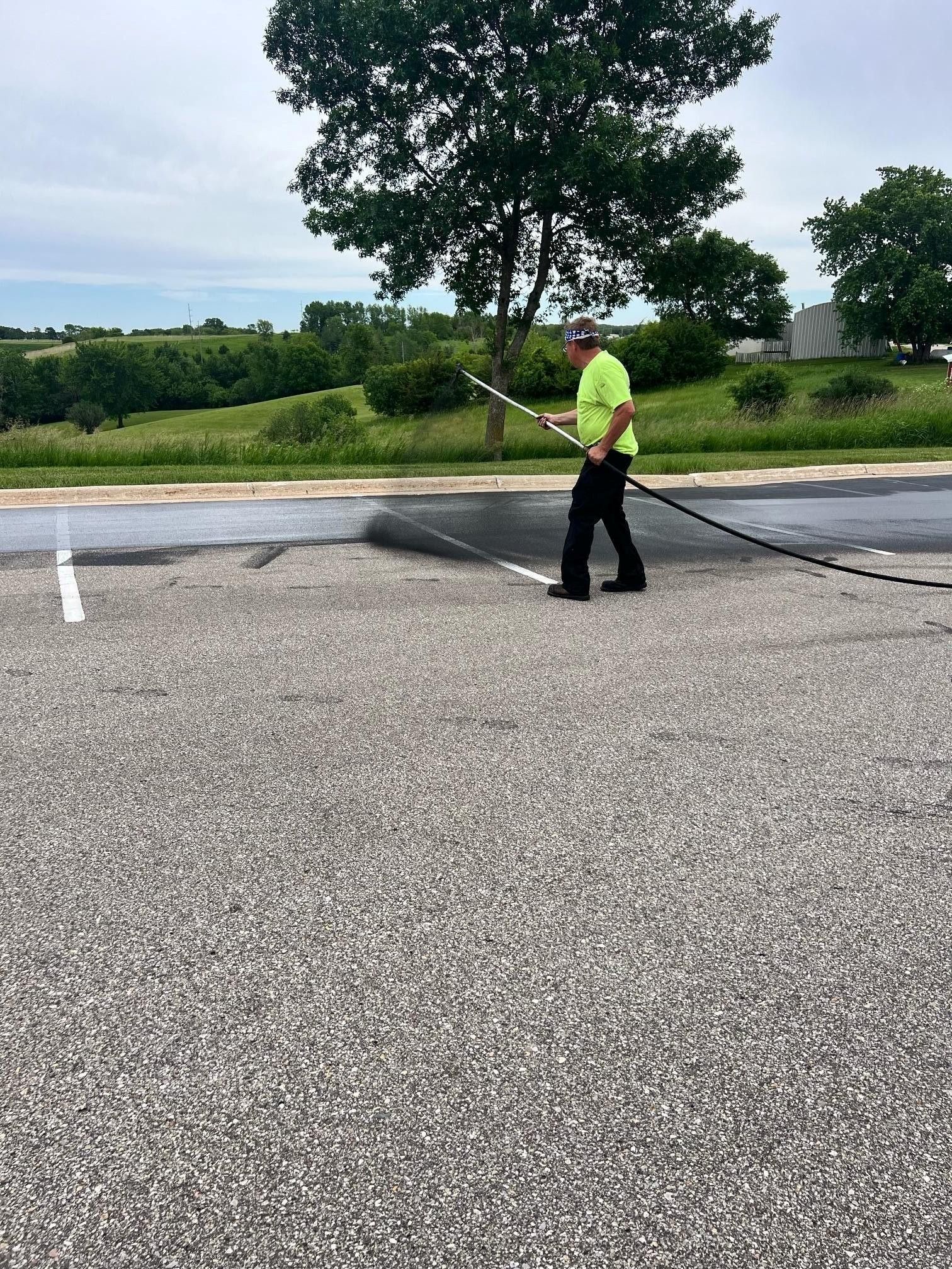 Gloved hand using a brush to apply thick black sealant to a gray road surface. Gloved hand using a brush to apply thick black sealant to a gray road surface.