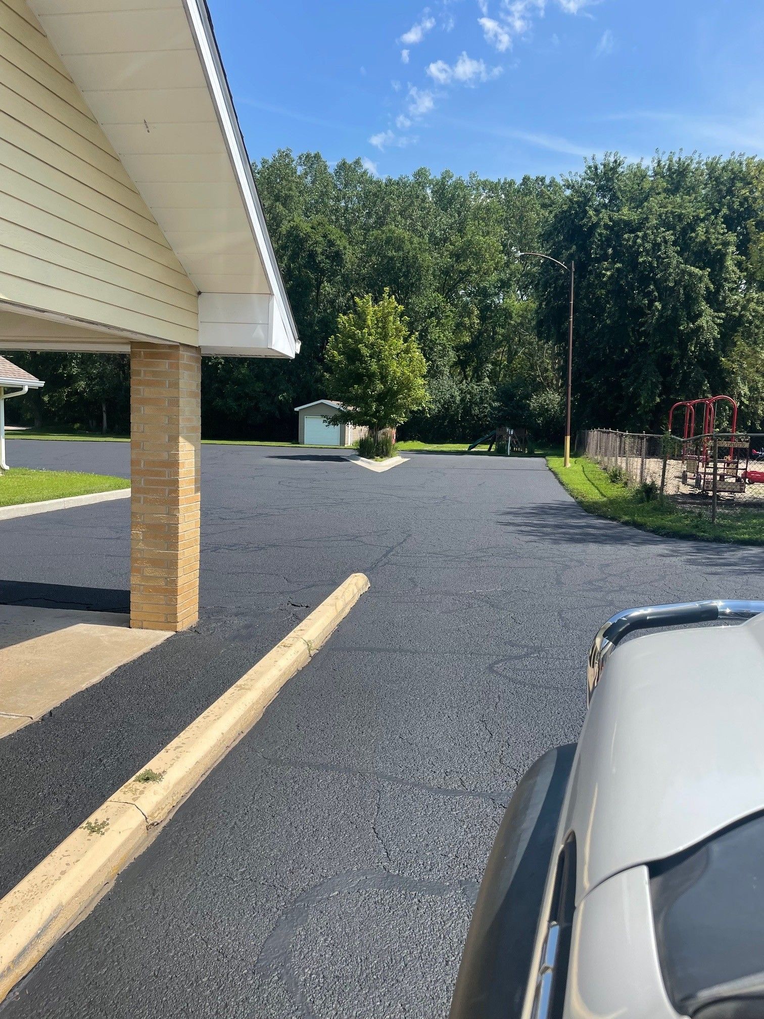 Freshly paved asphalt parking area next to a building and trees under a blue sky. Freshly paved asphalt parking area next to a building and trees under a blue sky.