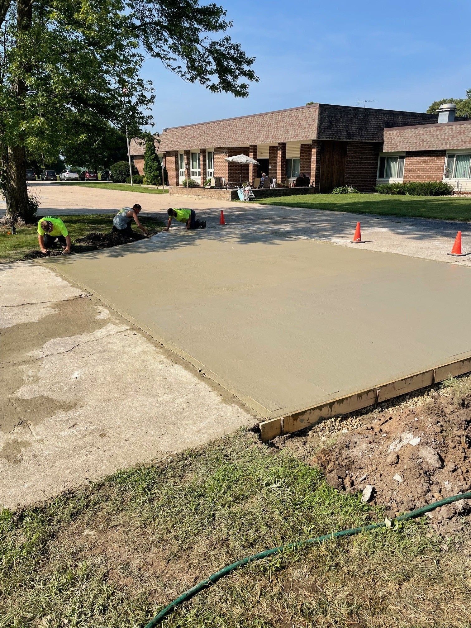 Workers pouring concrete driveway in front of a brick building. Workers pouring concrete driveway in front of a brick building.