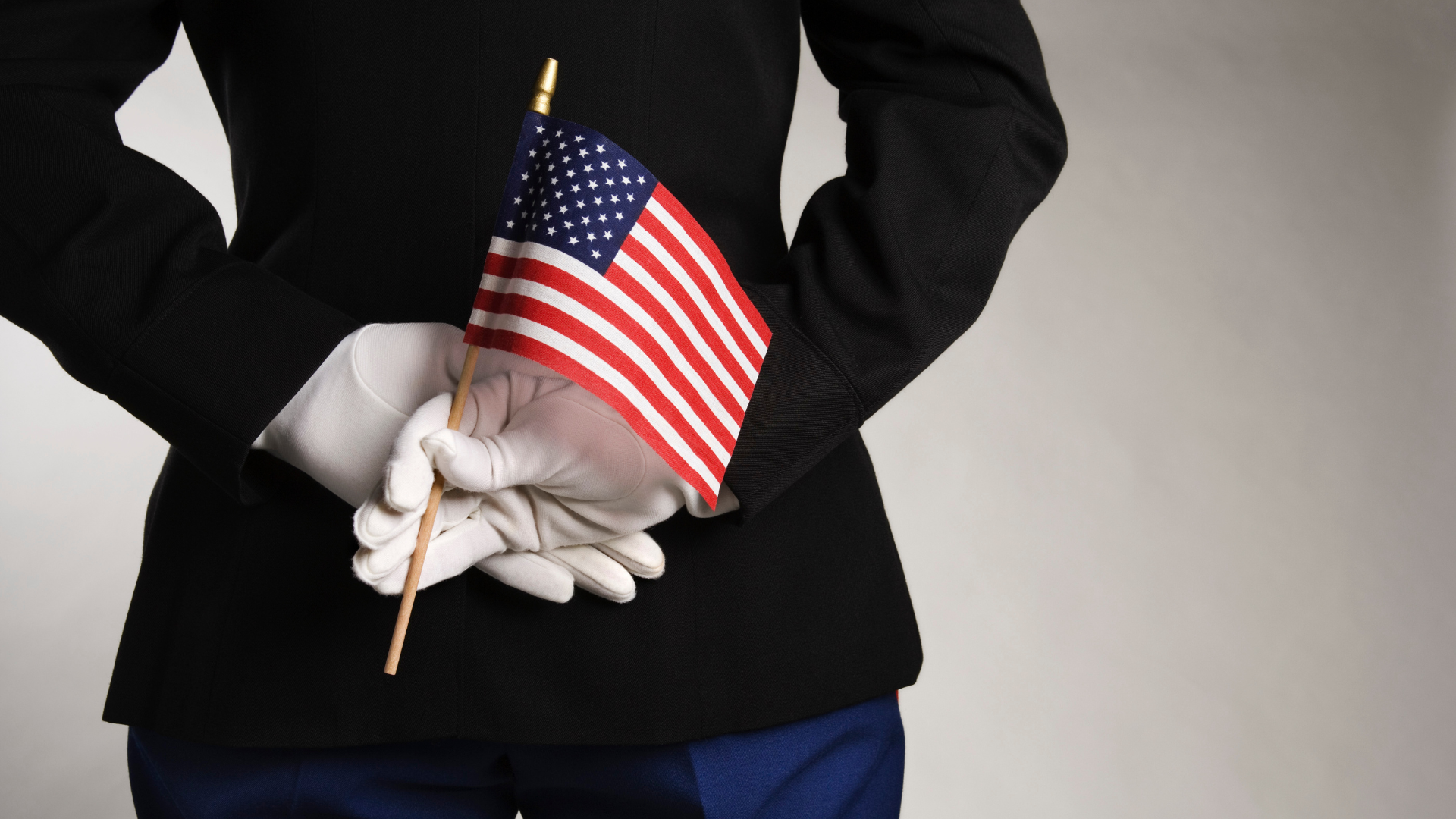 A man in a military uniform is holding an american flag behind his back.