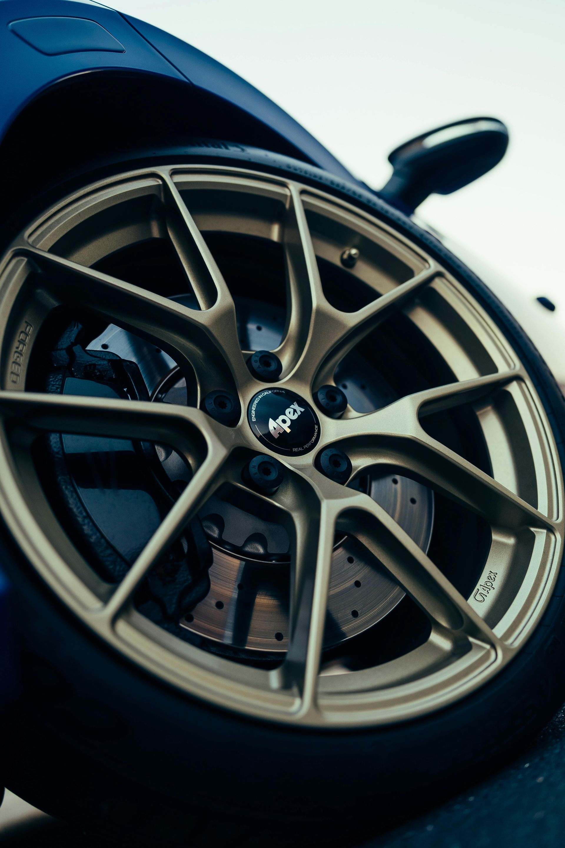Close-up of a gold alloy car wheel and brake disc on a dark blue sports car