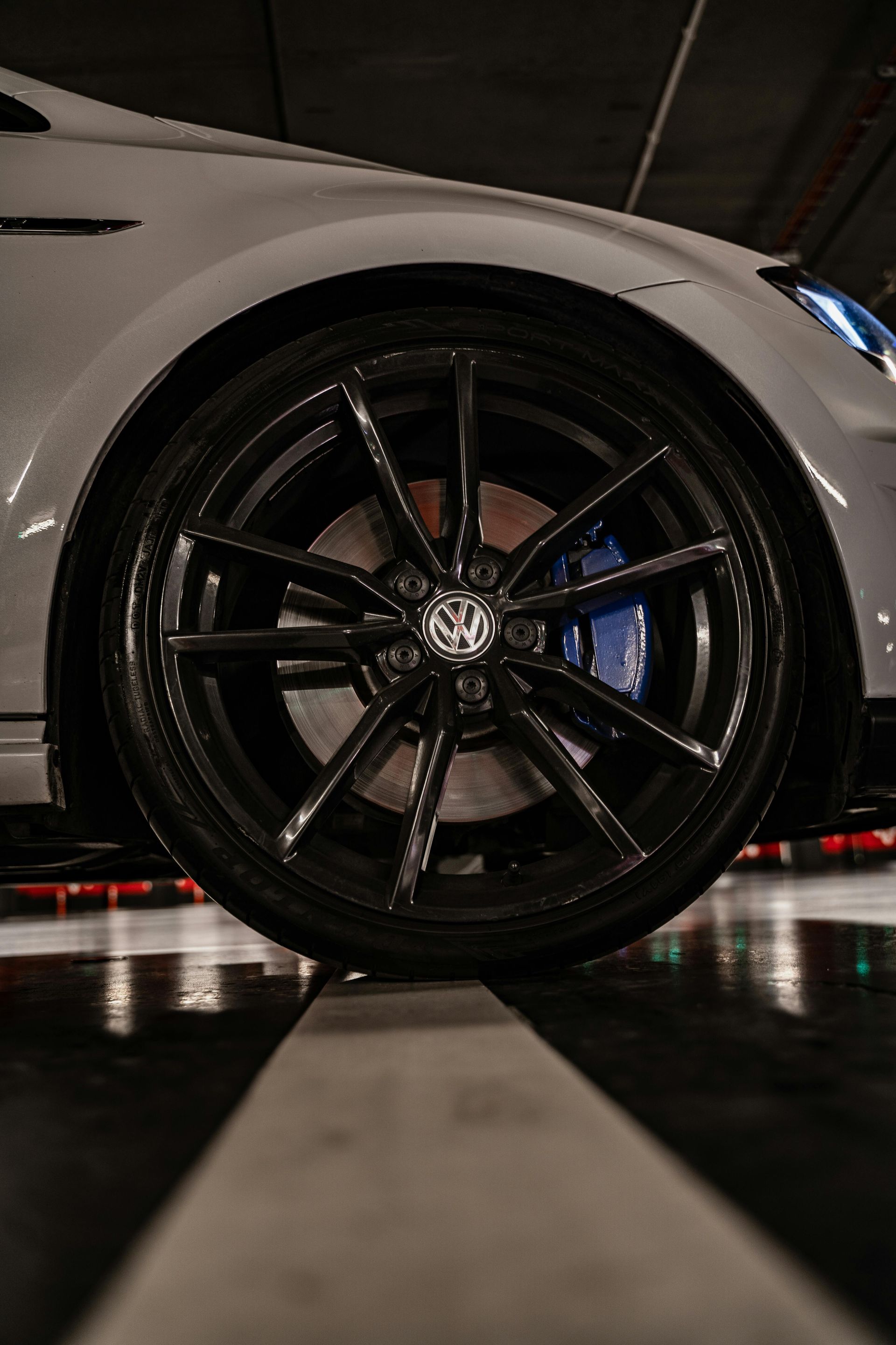 Close-up of a white sports car’s black alloy wheel in a dark garage, low-angle view.