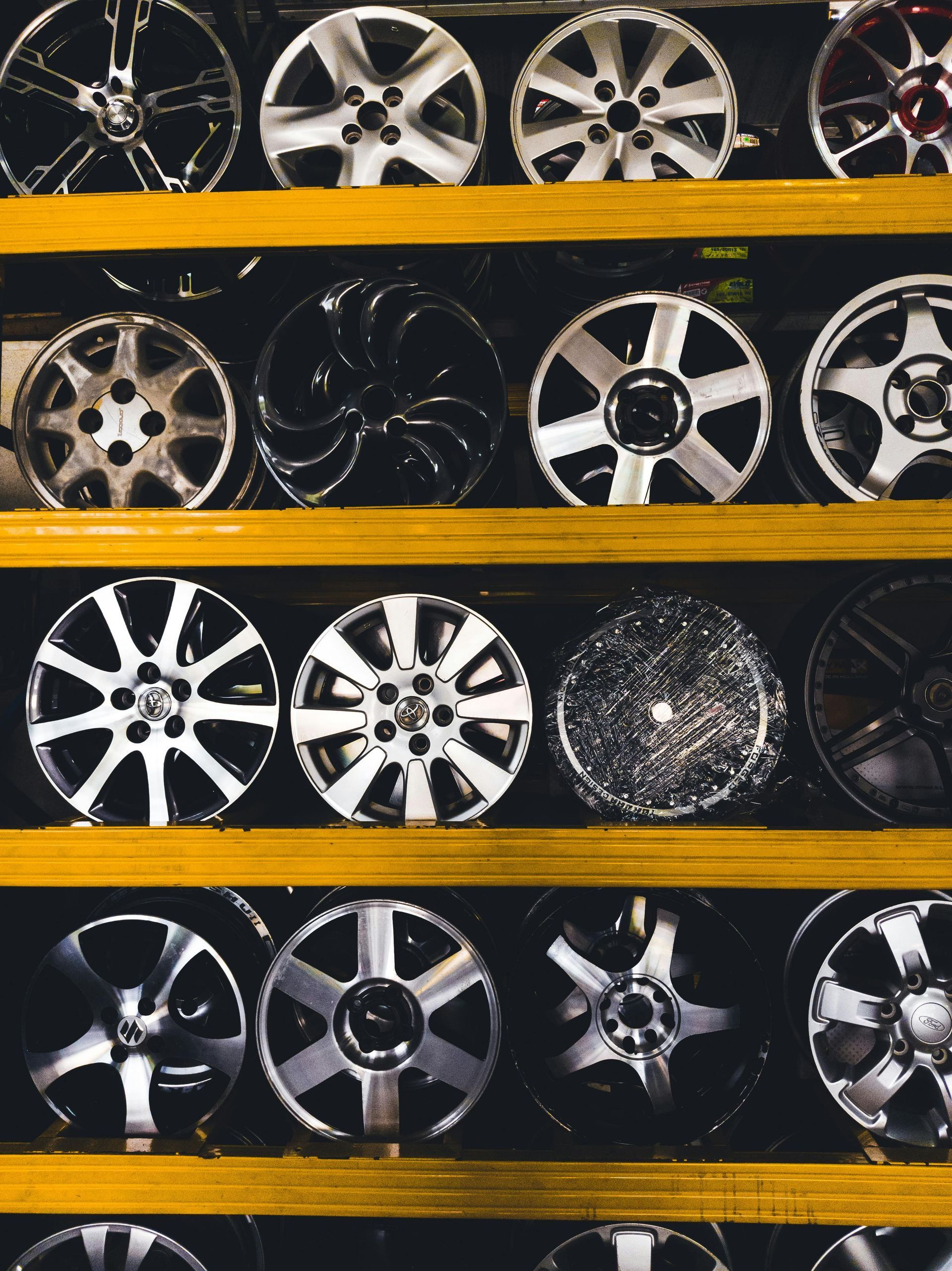 Rows of car rims and wheel covers displayed on shelves in a store, mostly silver and black.