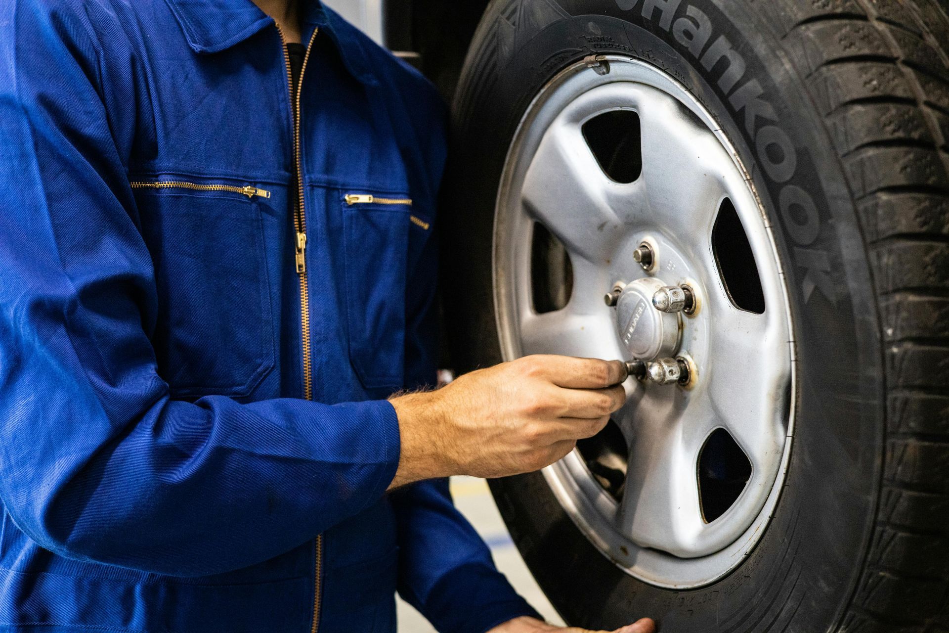 Mechanic in blue coveralls tightening lug nuts on a car wheel with a tire iron