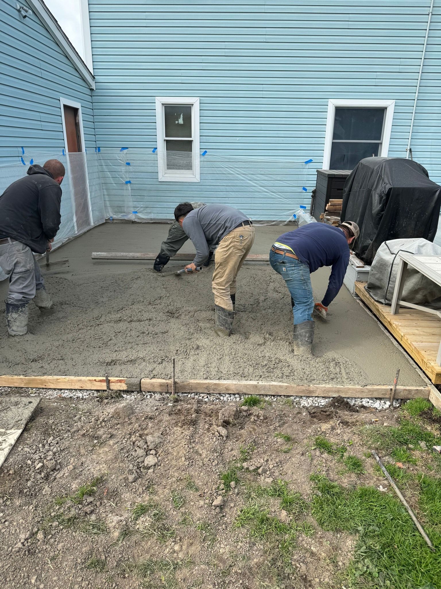 A group of men are working on a concrete patio in front of a house.