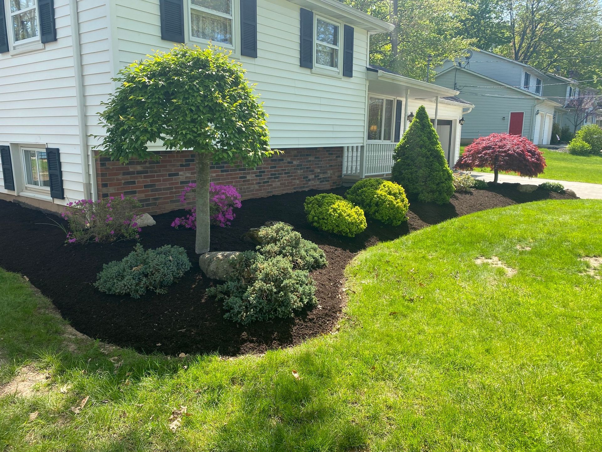 A white house with black shutters and a lush green lawn in front of it.