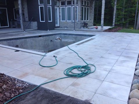 A hose is sitting on a tiled patio next to a swimming pool.