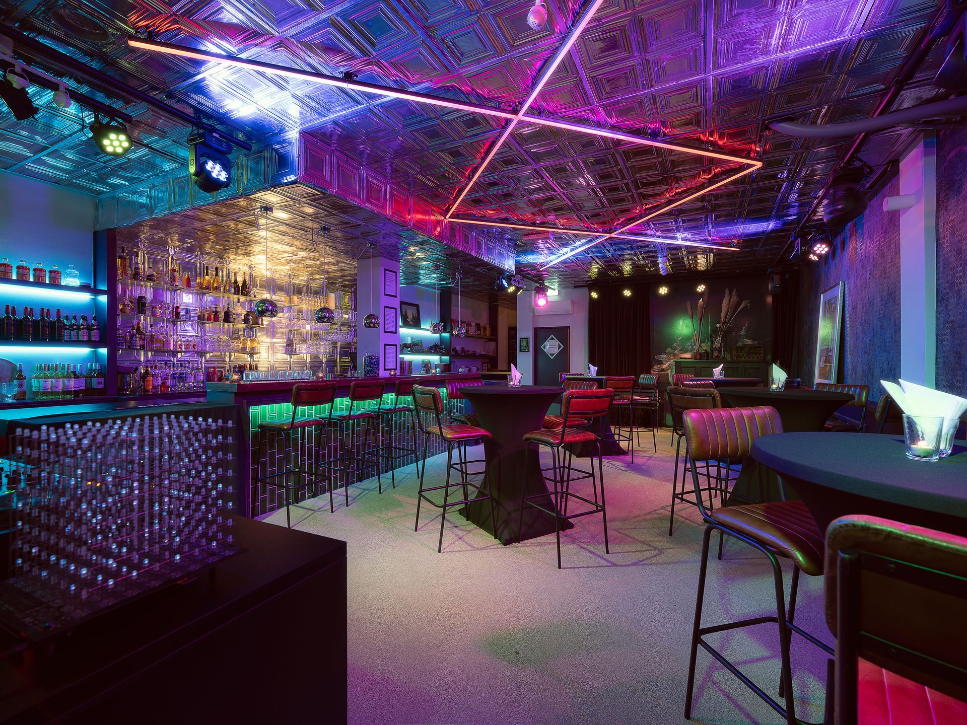 Bar interior with mirrored ceiling, colorful lights, and red bar stools.