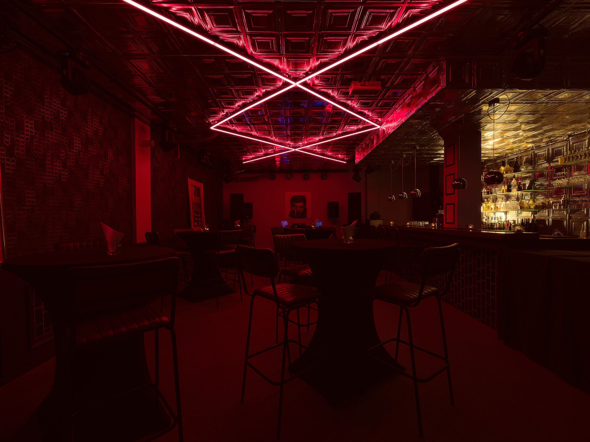 Red-lit bar interior with a diamond-shaped light fixture on the ceiling, stools, and a back-lit bar.