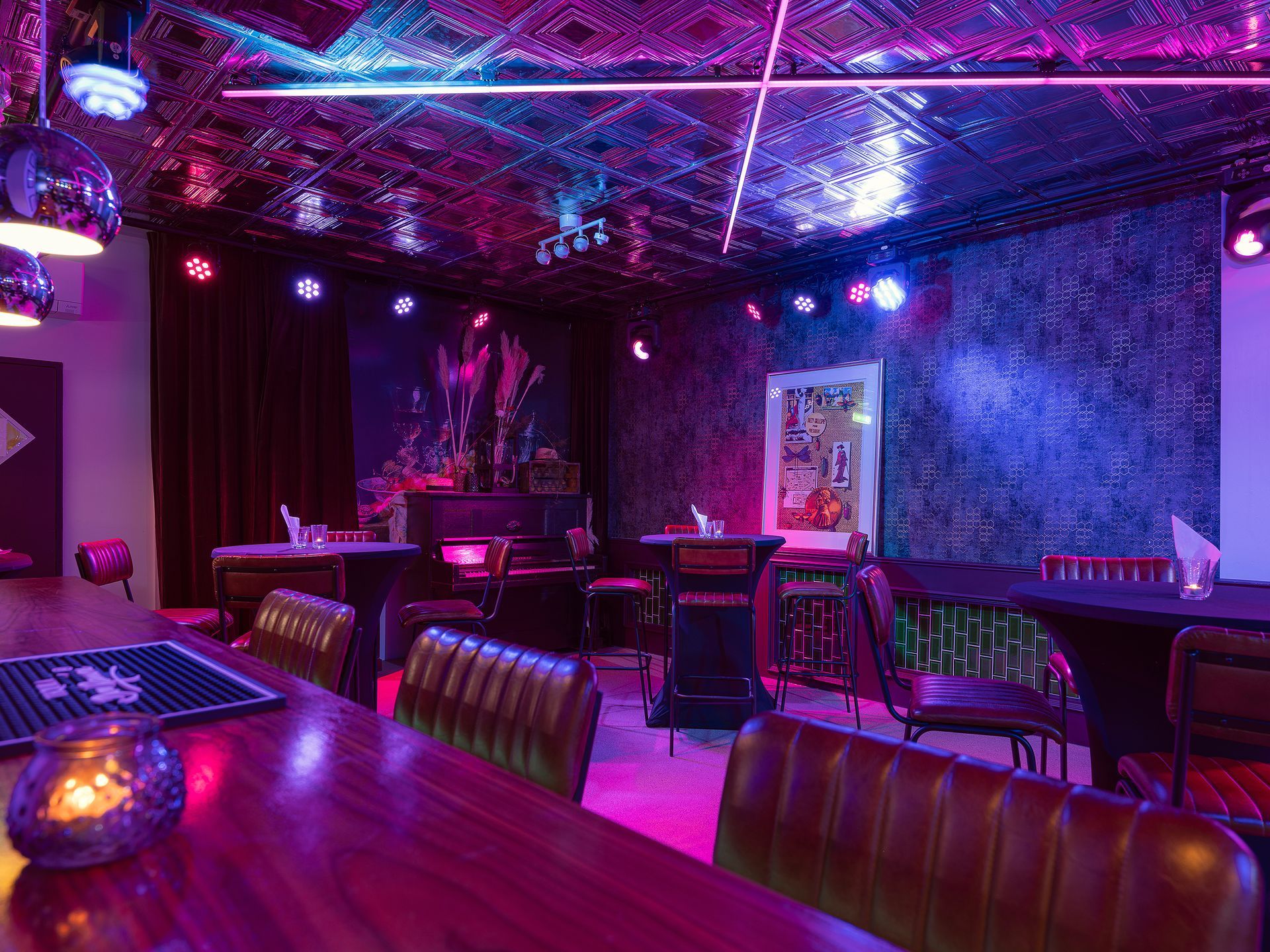 Interior of a bar with a stage, tables, and disco ball lighting. Purple and blue lights illuminate the room.