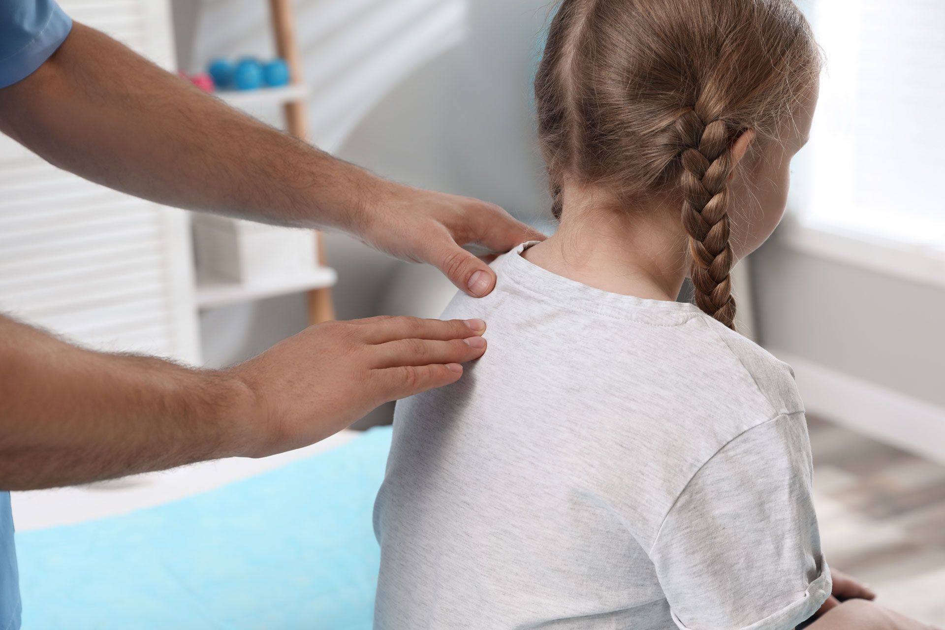 Chiropractor examining a child's back in a light-filled office.