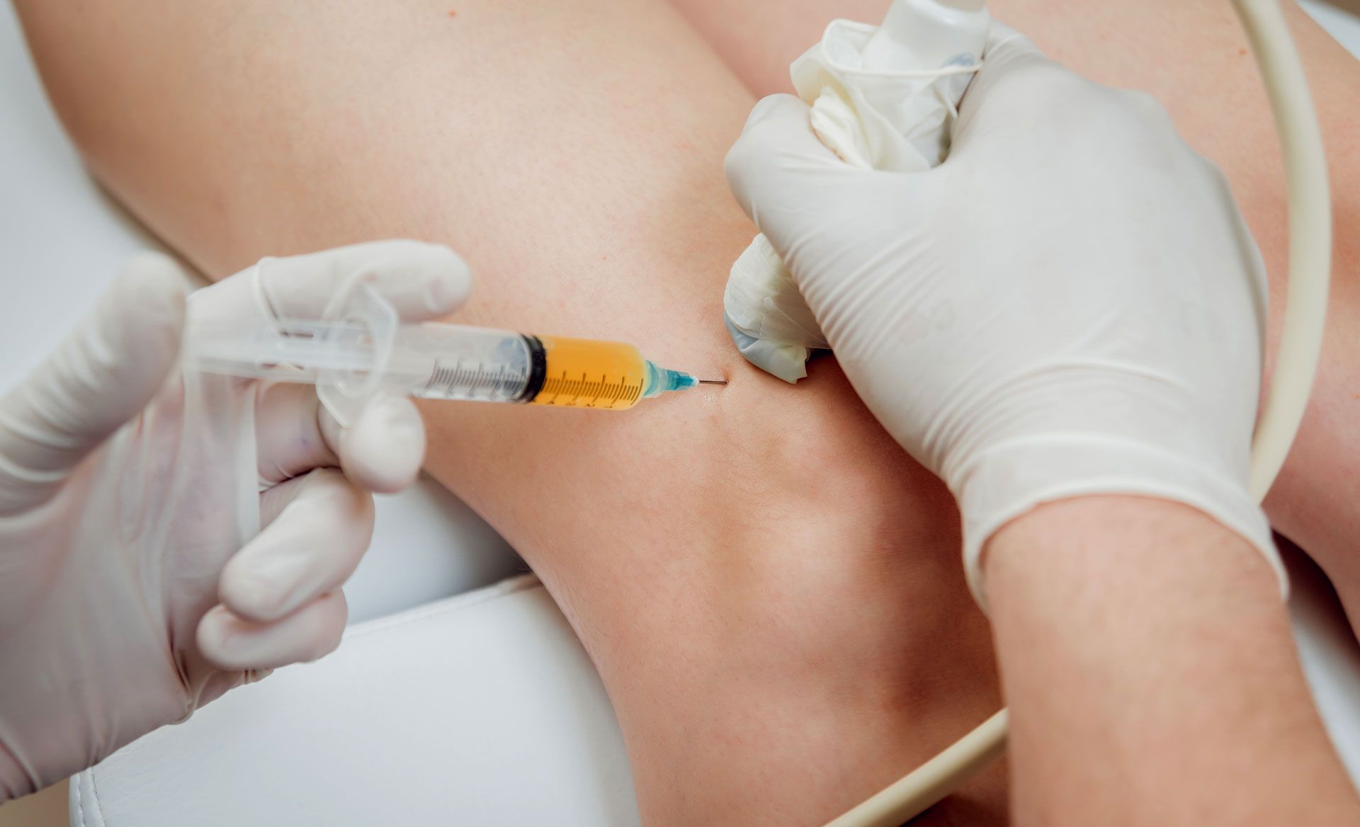 Hands in gloves injecting knee with a syringe.