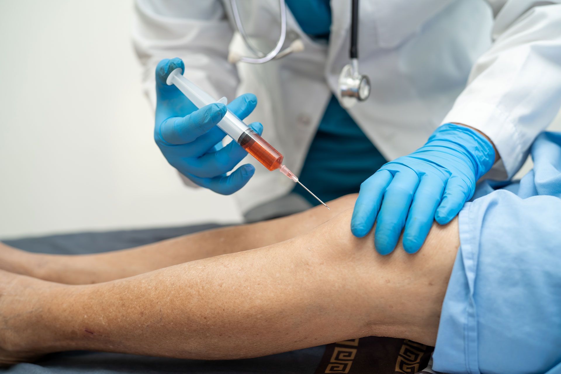 Doctor injecting fluid into a patient's knee with a syringe, wearing blue gloves.