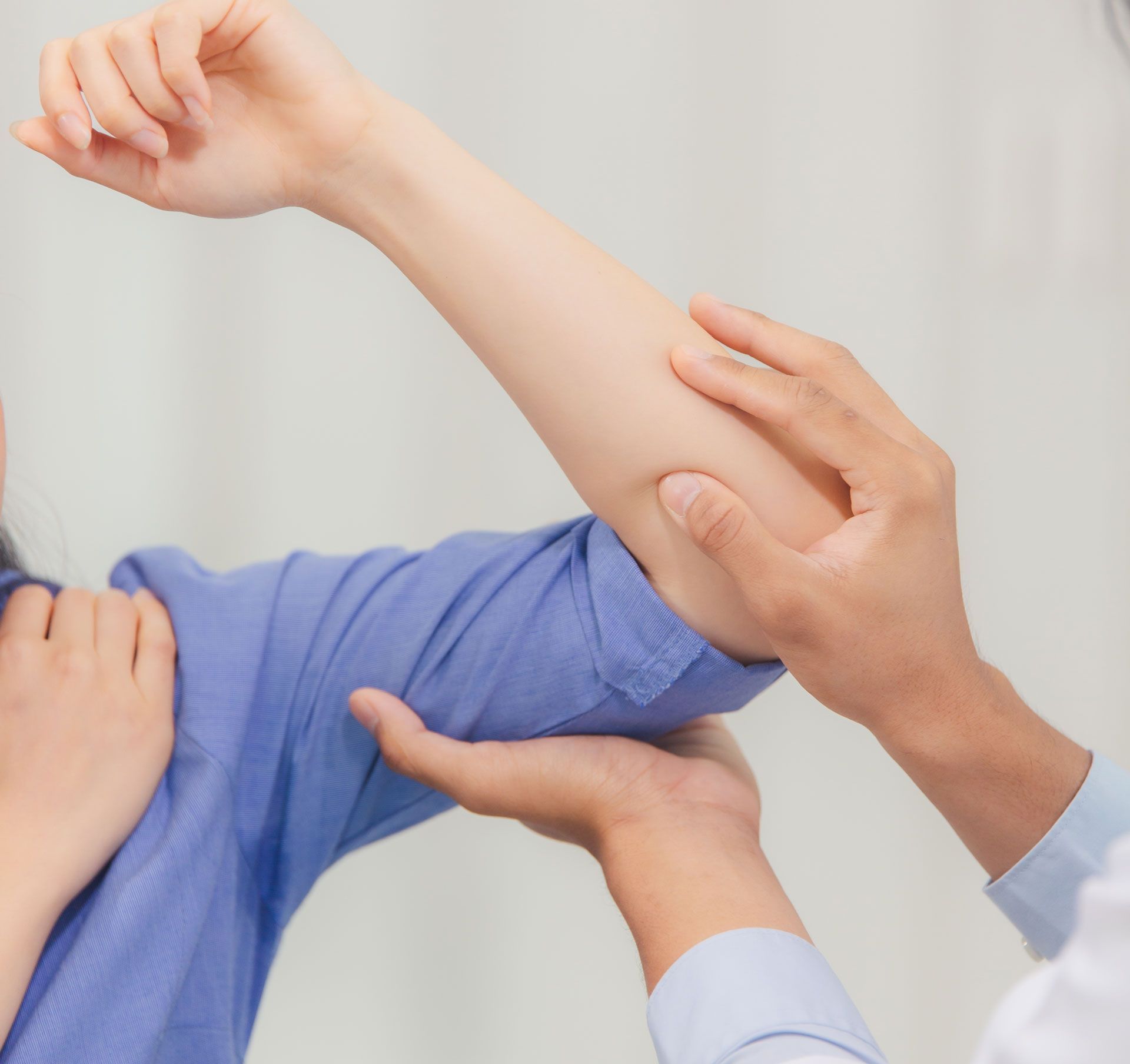 A person's arm being examined by a medical professional. The arm is bent at the elbow, and the hands are touching the arm.