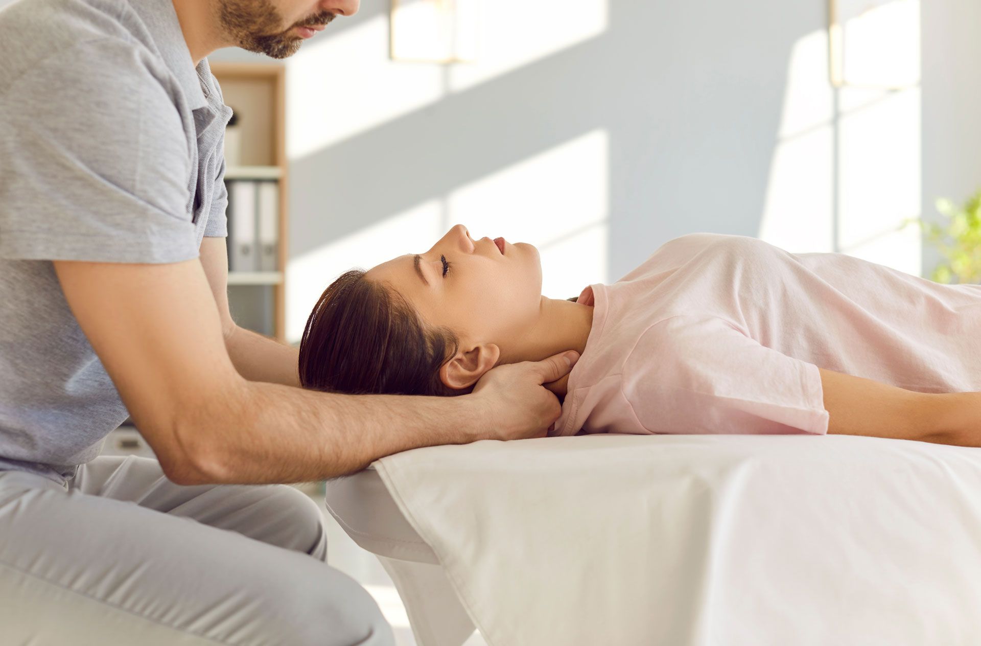 Man giving neck treatment to a person lying on a massage table. Indoor setting, daylight.