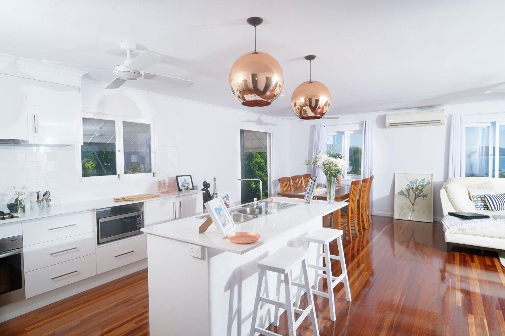 A Kitchen With White Cabinets, Wooden Floors, and Copper Pendant Lights — Pro-Jax Pty Ltd in Bohle, QLD