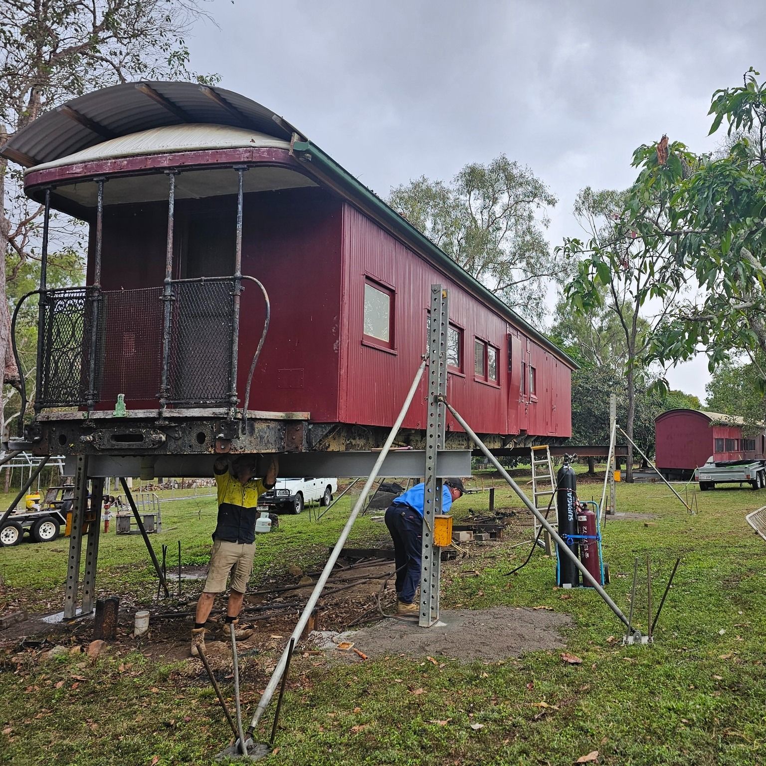 Workers Lifting and Leveling a Maroon Train Carriage on Metal Supports — Pro-Jax Pty Ltd in Bohle, QLD