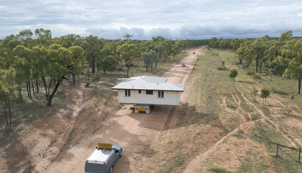 A House Being Transported on a Trailer Down a Dirt Road Lined With Trees — Pro-Jax Pty Ltd in Bohle, QLD