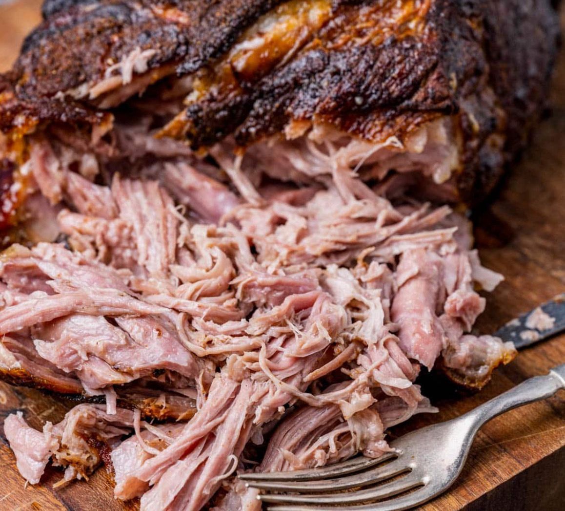 Pulled pork is sitting on a wooden cutting board with a fork.