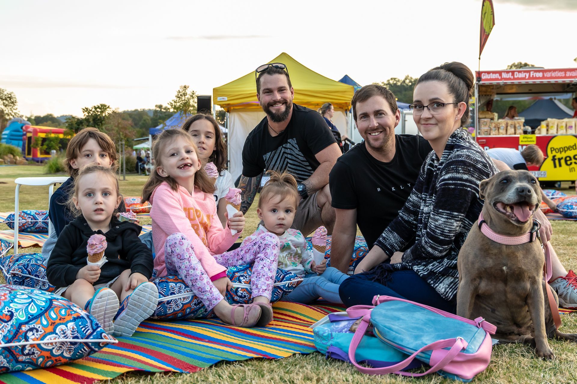 a group of people and a dog are sitting on a blanket in the grass .