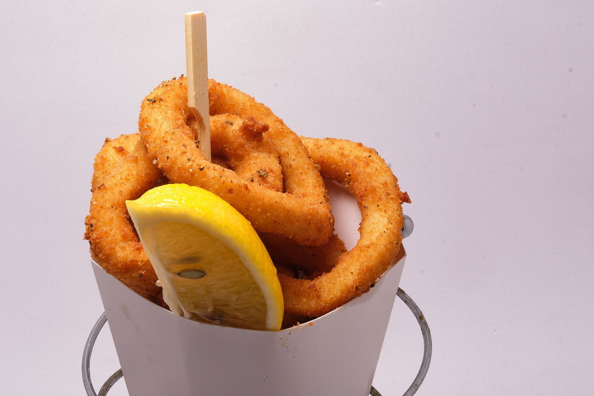 a cup of onion rings with a slice of lemon on a stick