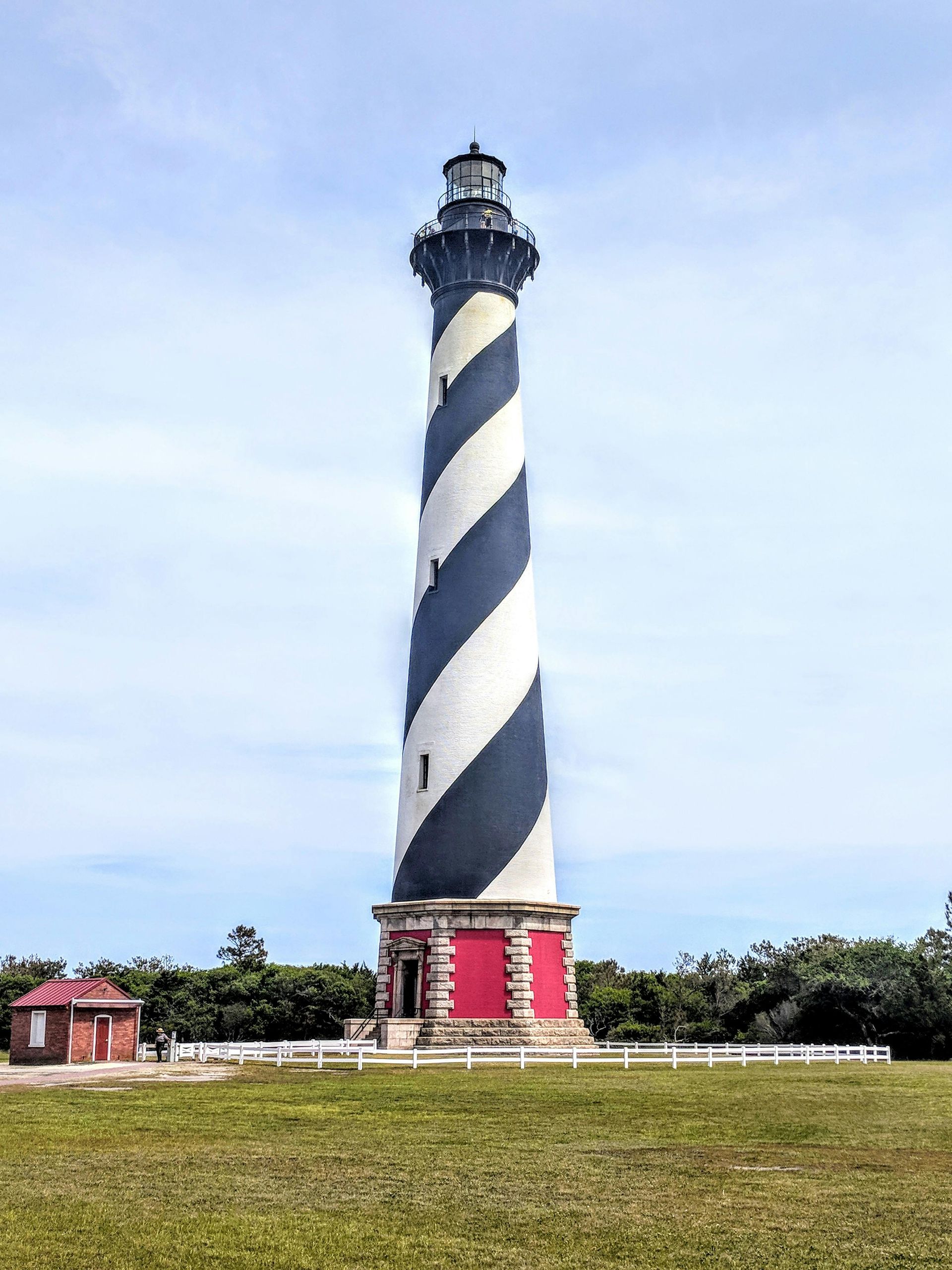 A black and white striped lighthouse is sitting in the middle of a grassy field.