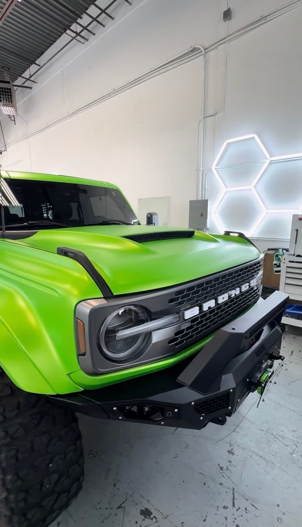 Bright green off-road SUV in a garage, front view with hexagonal wall lights behind it