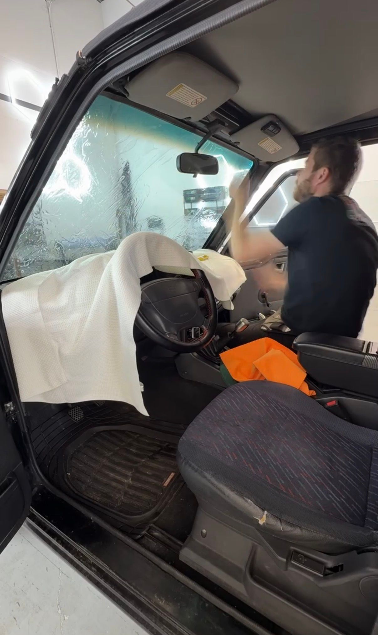 Person cleaning the interior of a car with white cloths and an orange tool bag.