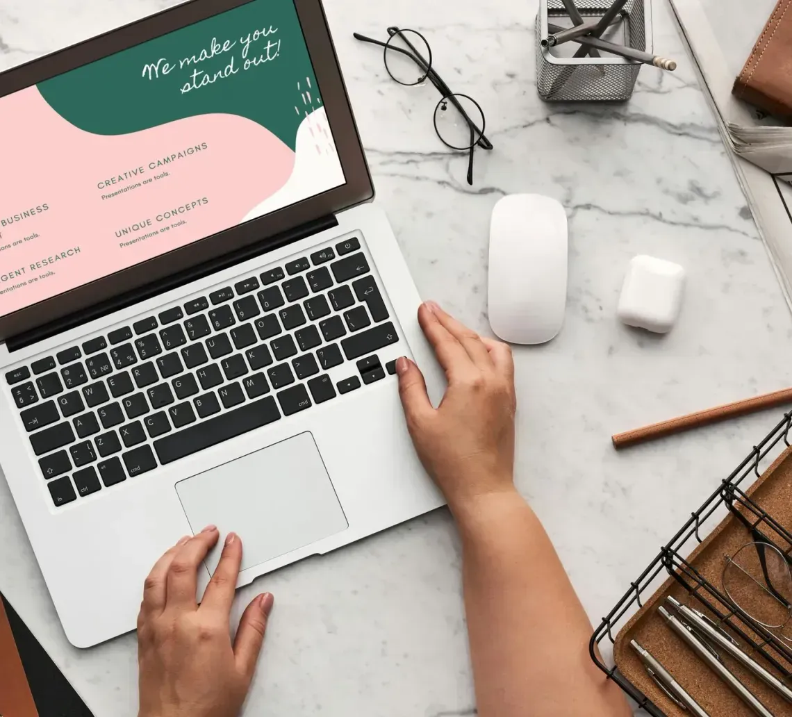 Laptop with hands, desk with office supplies, and a website on screen.