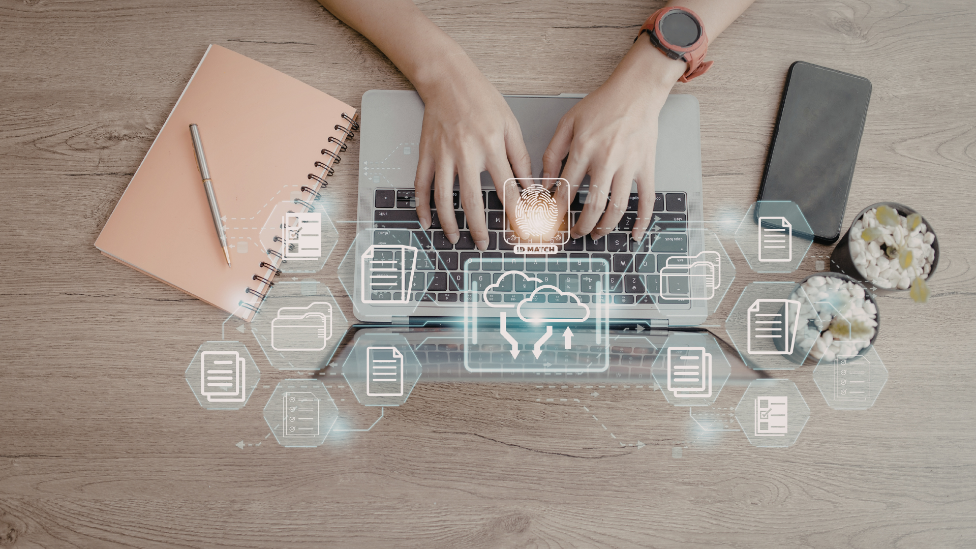 Hands typing on a laptop with cloud data icons overlaid on a wooden desk with a notebook, pen, phone, and plant.