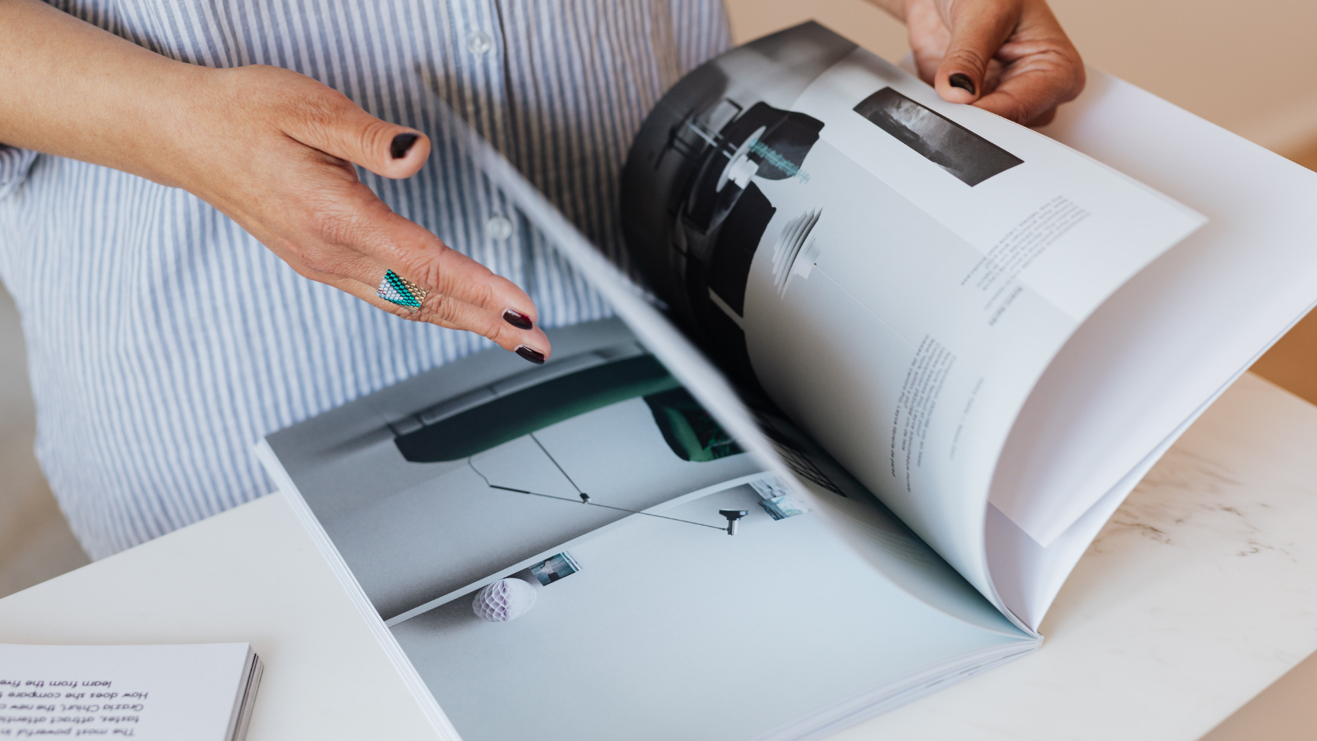 Hands flipping through a magazine with architectural interior photos on a white table.